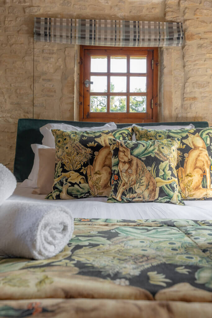 Lit double de la chambre Donjon avec coussins décoratifs et murs en pierre